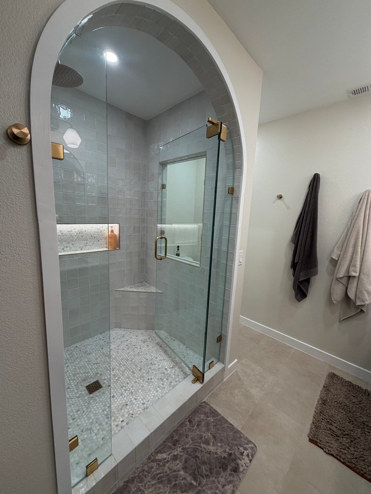 Wide view of a finished arched shower with glass enclosure and brass hardware