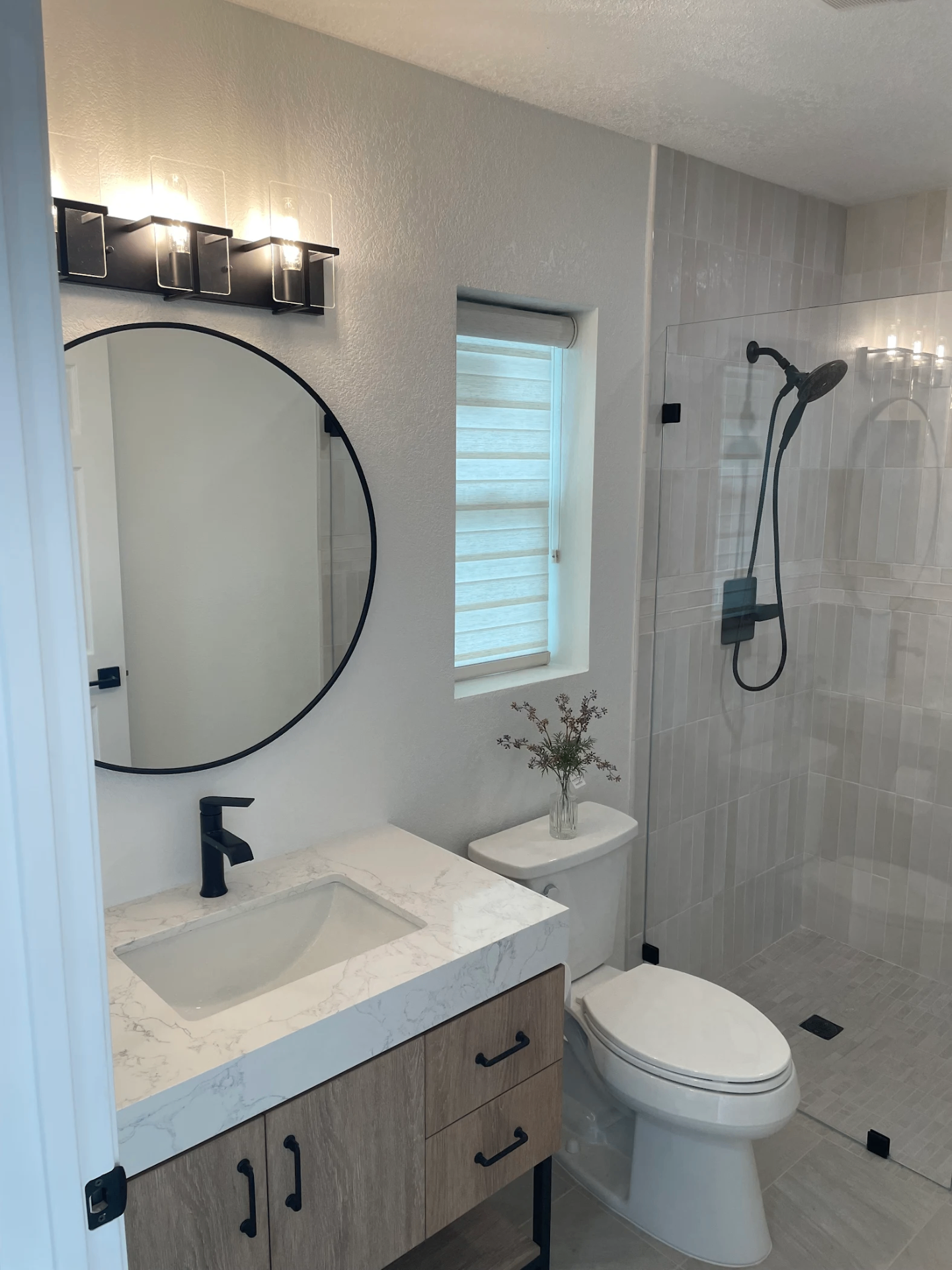 Remodeled bathroom with round mirror, quartz vanity, and tiled walk-in shower